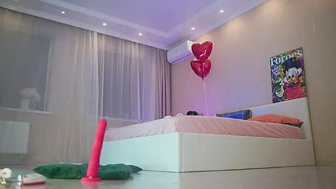 Media: Video of a modern, minimalist bedroom with a white bed, red heart balloons, and a colorful Disney poster on beige walls.