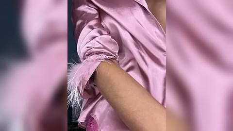 Media: Video of a person in a light pink satin robe with a feather accent on the right sleeve, the background is blurred.