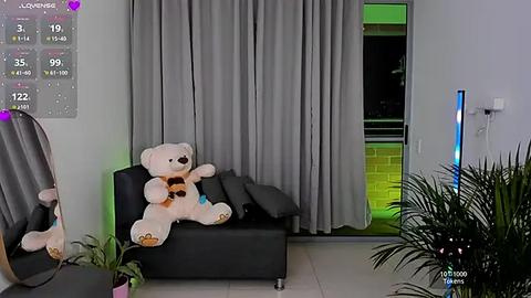 Media: A video of a modern living room with a plush white teddy bear on a black sofa, grey curtains, and a partially open door revealing a brick wall and a green light.