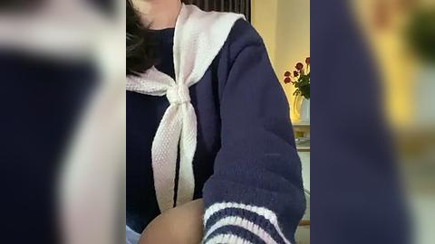 Media: Video of a woman wearing a navy blue sailor-style top with a white knitted scarf and red flower in the background.