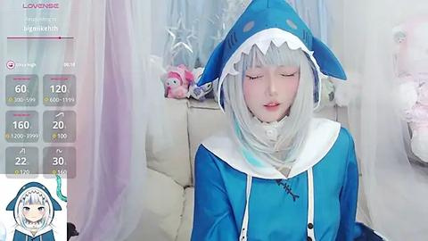 Media: Video of a pale-skinned person in a blue shark-themed cosplay, with long silver hair and closed eyes. Background features a pink and white room with a plush toy.