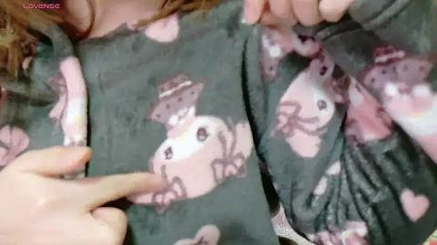 Media: A video of a person wearing a gray pajama top with a cartoon bear pattern, holding the top with both hands. The pajamas have a soft, plush texture.