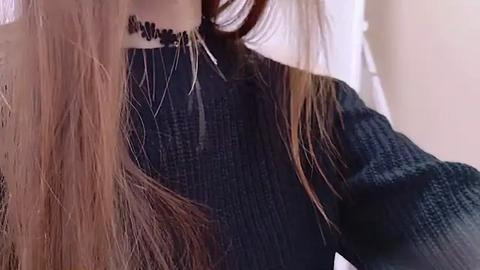 Media: Video of a person with long, straight, light brown hair, wearing a dark navy blue, textured sweater with a high neckline and a black choker necklace.