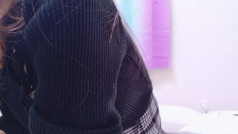 Media: Video of a woman's backside in a black, ribbed sweater, with long, wavy brown hair, and a blurred background featuring a lavender and blue gradient wall.