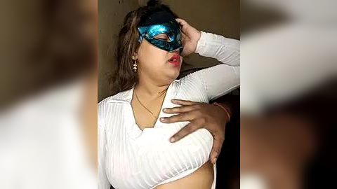 Media: Video of a woman with medium brown skin, wearing a sheer white top, a blue eye mask, and red lipstick, posing seductively against a plain background.