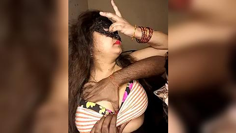 Media: Video of a South Asian woman with long black hair, wearing a colorful striped top, blindfold, and multiple bracelets, being embraced by a man.