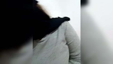 Media: A video capturing a person's back in a gray sweater and black scarf, partially obscured by a blurred, black-haired figure in the foreground. The background is plain white, creating a stark contrast.