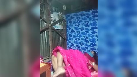 Media: A blurry video of a young child lying on a bed, partially covered by a pink blanket, in a room with blue patterned walls and wooden furniture.