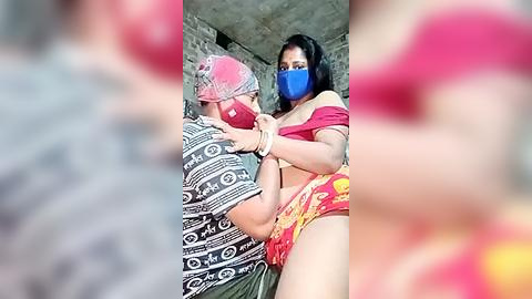 Media: Video of a woman in a red saree and blue mask being carried by a man in a patterned shirt, both in a rustic setting with blurred background.