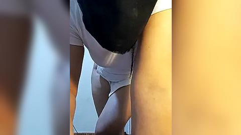 Media: Video of a woman in a tight white leotard, leaning forward with her back arched, black hair partially covering her face.