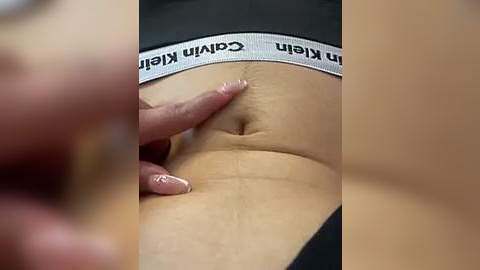 Media: A close-up video shows a person's stomach with a hand gently touching the navel, wearing Calvin Klein underwear. The background is blurred, highlighting the skin texture and underwear branding.