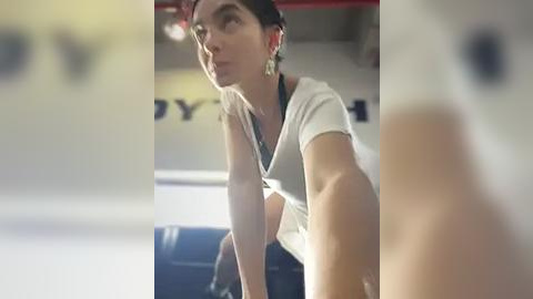 Media: A video shows a woman with dark hair, wearing a white top, and looking contemplative, possibly in a gym or workout area.