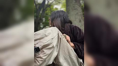 Media: A video shows two people embracing in a forest; one with long dark hair and a brown coat, the other with light hair and beige jacket. The background features blurred green trees.