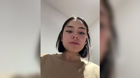 Media: A video of a young woman with straight, shoulder-length black hair, light skin, and a slight smile. She wears a beige t-shirt indoors against a plain white wall.