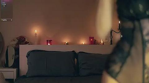 Media: A dimly-lit video of a cozy bedroom with a white bed, dark pillows, lit candles, and a black lace curtain in the foreground.