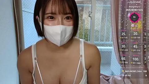 Media: Video of an East Asian woman with short black hair, wearing a white mask and spaghetti-strap top, standing indoors by a window. A live-streaming app screen overlays her image with viewer stats.