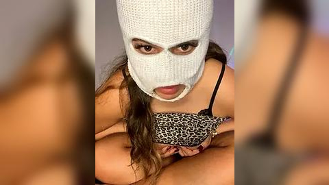 Media: Video of a woman with medium skin tone, wearing a white balaclava and leopard-print bra, looking seductively.