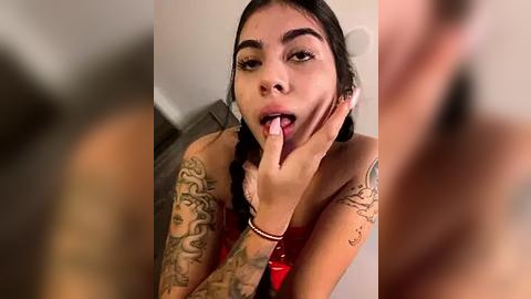 Media: Video of a Latina woman with long black hair, medium skin tone, and tattoos on her arms, licking her finger suggestively, wearing a red dress.