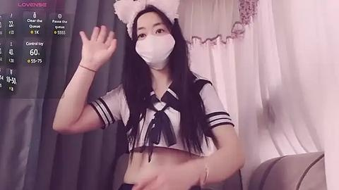 Media: A video of an Asian woman in a white crop top with black bow, white cat ears, and mask, waving in a dimly lit room with sheer curtains.