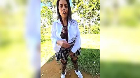 Media: A video of a woman in a plaid skirt and fishnet stockings, crouching on a dirt path, surrounded by lush greenery. She has long dark hair and a distressed expression.