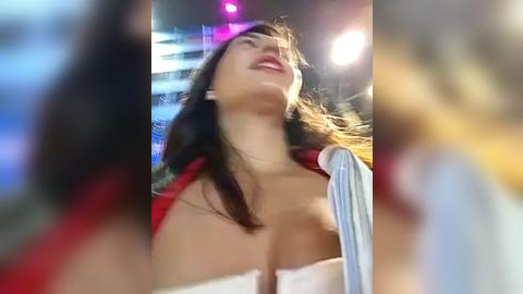 Media: Video of a young woman with long brown hair, fair skin, and medium-sized breasts, wearing a white strapless top and a red jacket, dancing joyfully under colorful nightclub lights.