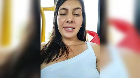 Media: Video of a Latina woman with medium brown skin, straight dark hair, and brown eyes, wearing a white one-shoulder top, smiling, seated on a bus with blurred passengers in the background.