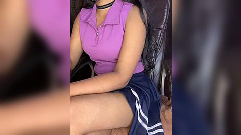 Media: Video of a woman with medium skin tone wearing a purple sleeveless polo shirt and navy blue athletic shorts with white stripes, sitting on a black office chair.