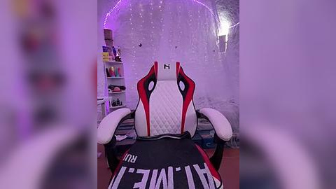 Media: Video of a gamer sitting in a white and black gaming chair, facing a wall adorned with LED lights and a bookshelf.