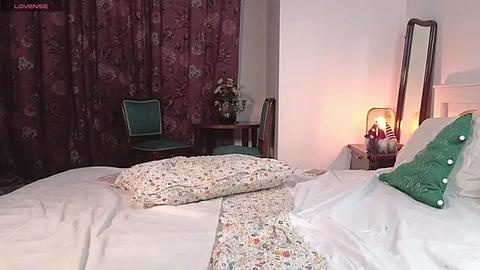 Media: Video of a vintage bedroom with a floral bedspread, green pillow, wooden chair, floral curtains, and a mirror, warm lighting, and retro decor.
