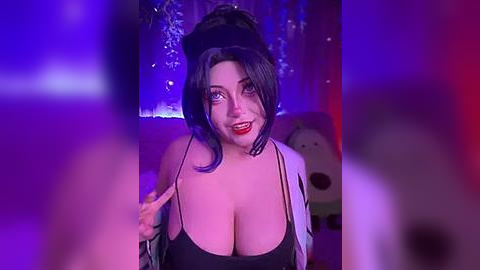 Media: Video of a woman with large breasts in a black tank top, wearing dramatic makeup and a black wig, standing in front of a purple and blue backdrop with a teddy bear.