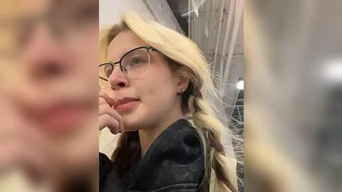 Media: Video of a young woman with glasses, blonde pigtails, and a black shirt, wearing a clear plastic mask that partially covers her face.