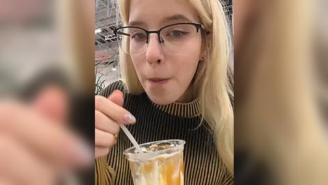 Media: Video of a young blonde woman with glasses, wearing a black and white striped sweater, sipping from a glass of tea.