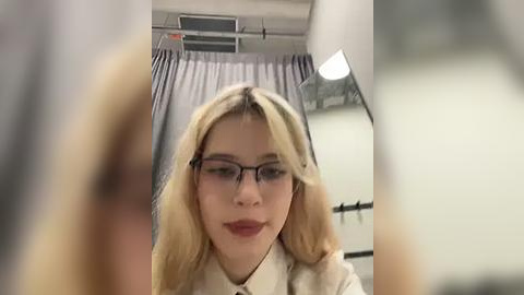 Media: A video of a blonde woman with glasses, fair skin, and light makeup, wearing a white blouse, seated in an airplane cabin.