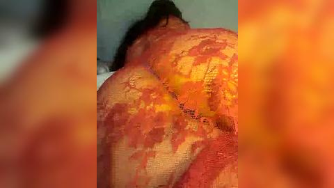 Media: Video of a woman's backside, covered in bright orange paint, with visible texture, in a dimly lit room, blurred background.