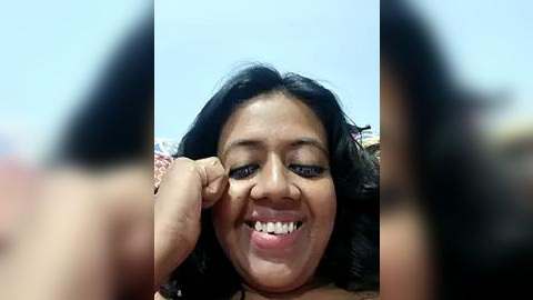 Media: A video of a smiling, middle-aged woman with long, dark hair, wearing a patterned top, and a blurred background. She is playfully sticking her tongue out, captured in a casual, candid moment.