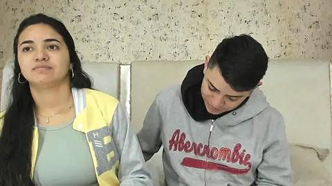 Media: Video of a young Hispanic woman with long black hair in a yellow jacket, sitting next to a young Hispanic man with short black hair in a grey hoodie, both looking solemn.