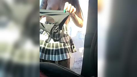 Media: A video of a person wearing a green plaid skirt, holding a black purse, reflected in a car mirror. The background is blurry.