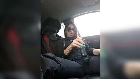 Media: Video of a man in sunglasses and black hoodie, seated in a car with a black bag beside him, holding a green bottle.