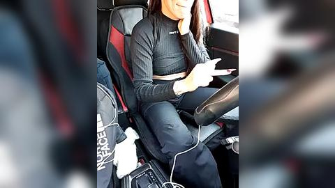 Media: Video of a woman with light skin, wearing a black crop top and leggings, seated in a car. She is using a cell phone and has a bottle of water beside her.