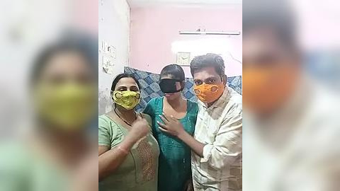 Media: Video of three masked people in a bathroom, two women and one man, wearing yellow and orange masks, standing close together, with blue and white tiled walls in the background.