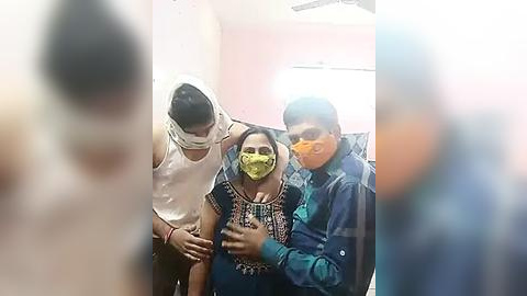 Media: Video of a woman in a yellow mask, seated in a room with two men; one wearing a white mask and another in a blue jacket.