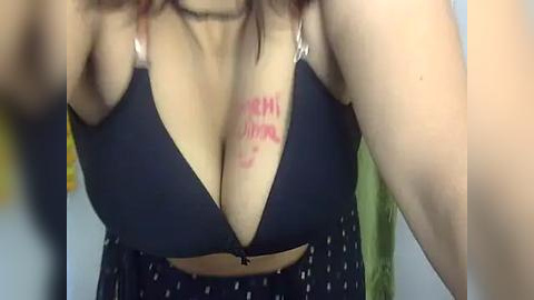 Media: Video of a woman with fair skin and a curvy physique, wearing a black polka-dotted bra, revealing cleavage with \"MOMMA I'M GONNA F*CK YOU\" handwritten in red on her left breast.