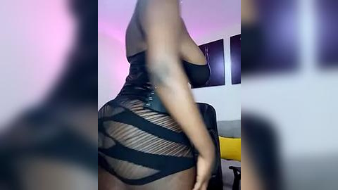 Media: Video of a curvy Black woman in a revealing black mesh dress, accentuating her large breasts and ample hips. Background shows a modern, dimly lit room with purple and pink lighting.