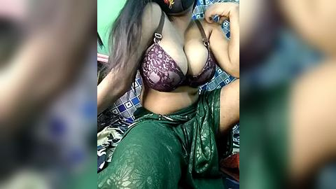 Media: Video of a woman with long black hair, wearing a purple lace bra and green pants, sitting on a bed with blue and white patterned sheets.