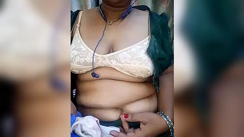 Media: Video of a South Asian woman with medium brown skin, wearing a white lace bra and a green blouse, holding a stethoscope to her chest. She has a plump figure, red nail polish, and a silver bracelet on her wrist.