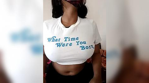 Media: Video of a woman with medium-dark skin and long dark hair, wearing a white crop top with \"First Time You Were Born\" printed in blue, and a plaid skirt.