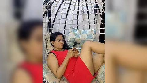 Media: Video of a woman with medium skin tone, wearing a red dress, lying in a white macram\u00e9 swing, reading a book, surrounded by blurred figures.