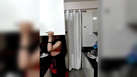 Media: Video of a woman with long brown hair, wearing a red bra and black wristband, in a bathroom with a white shower curtain, black sink, and mirror.