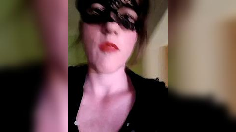 Media: Video of a person wearing a black lace mask, red lipstick, and black top, with blurred background, creating a mysterious, slightly distorted, and intimate atmosphere.