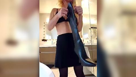 Media: Video of a blonde woman with a flat stomach, wearing a black bra and skirt, holding a blue fish in a modern bathroom with beige tiles and a white sink.